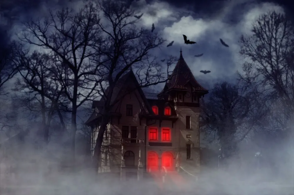 Haunted house on a hill with red lights shining inside and bats flying overhead